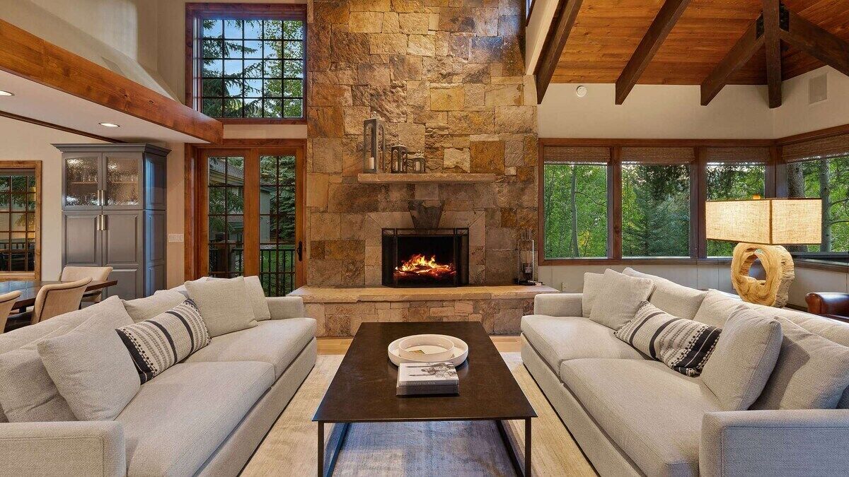 A cozy living room with a stone fireplace, two sofas, a coffee table, and large windows.