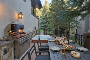 An outdoor patio with a grill, hot tub, and dining table set for a meal.