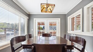 A dining room with a round table and six chairs, a chandelier, and large windows with blinds. - Peak House Hot Tub 3BR 2.5BA Close to Downtown  (Boise)