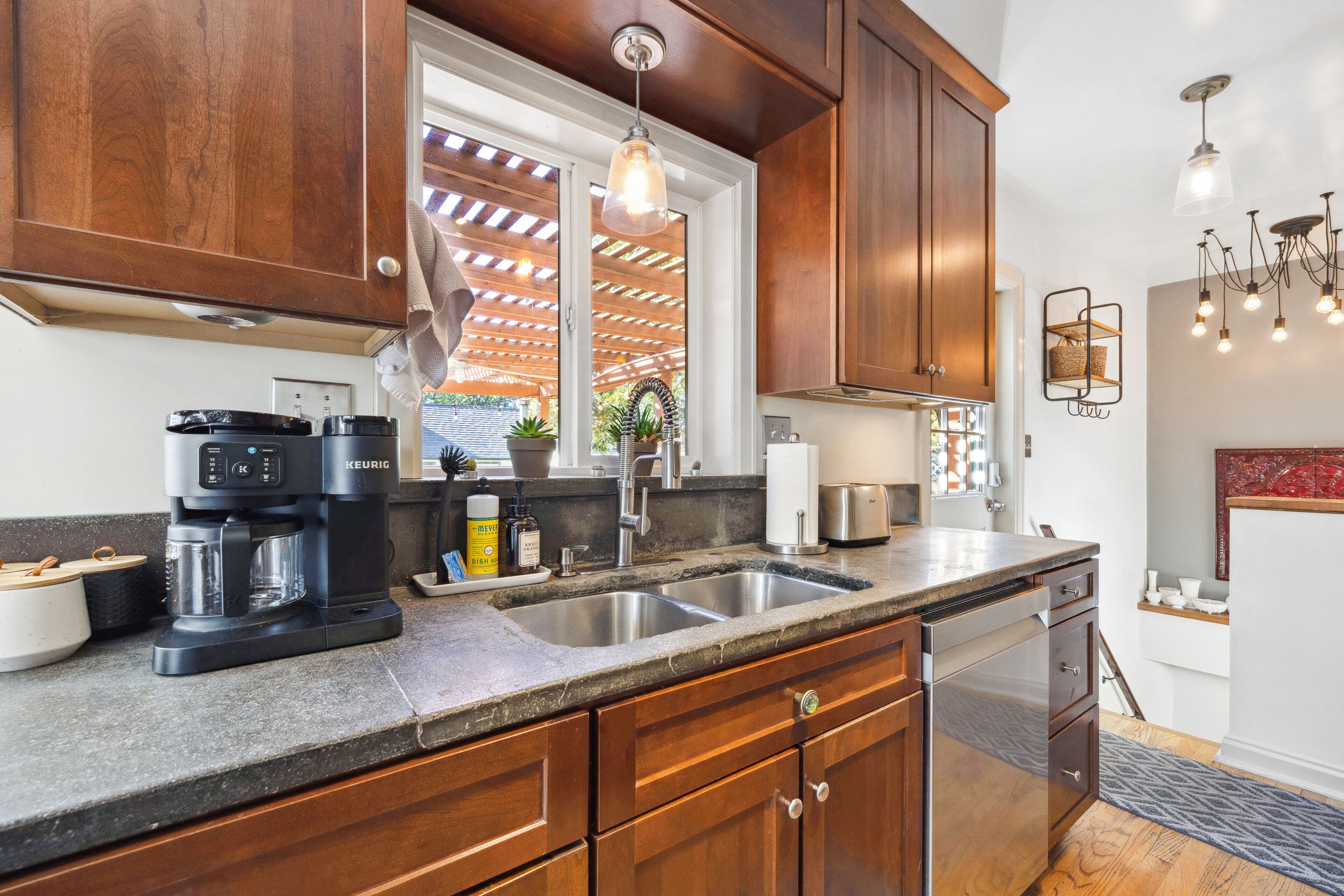 A kitchen with wooden cabinets, a stainless steel sink, a coffee maker, and a built-in dishwasher.