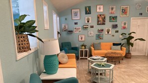 Uma sala de estar com móveis verde-água e laranja, uma porta branca e diversas obras de arte emolduradas nas paredes.