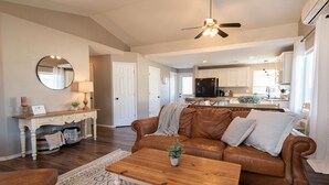 A spacious living room with a leather sofa, wooden coffee table, and a dining area with a kitchen in the background.