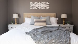 A neatly made bed with a patterned throw, two bedside tables with lamps, and a decorative wall piece.