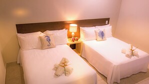 Een hotelkamer met twee bedden, elk voorzien van witte lakens en decoratieve kussens, een nachtkastje met een lamp en bloemen, en handdoeken netjes opgemaakt op de bedden.