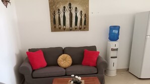 Un salon avec un canapé gris, des coussins rouges et beiges, une table basse agrémentée d’objets décoratifs et deux fauteuils blancs.