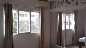 Une chambre avec un lit, un ventilateur de plafond, une porte-fenêtre coulissante et une vue sur les bâtiments environnants.