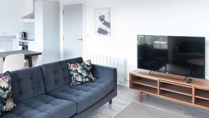 A modern living room with a sofa, a television, and a kitchen area in the background. - Newly Refurbished 2 bed with Fantastic View (London)