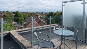 A rooftop terrace with a glass balustrade, a round table, two chairs, and a view of a residential area. - Newly Refurbished 2 bed with Fantastic View (London)