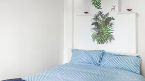 Quarto com uma cama, colcha listrada em azul e branco, manta azul e uma planta fixada na parede.