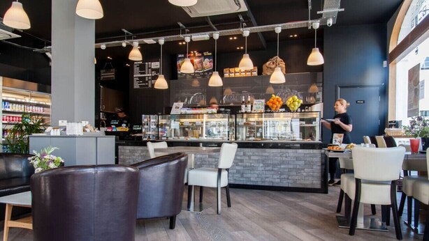 Um café moderno com mesas, balcão e quadro de ementa.