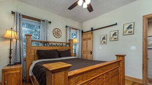 A bedroom with a wooden bed, two nightstands, a ceiling fan, and a window with patterned curtains. - Amazing! 2 Bed Townhouse in the HEART of Dbq! (Dubuque)