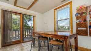 A dining area with a wooden table and two stools, a sliding glass door, and a window with blinds. - Amazing! 2 Bed Townhouse in the HEART of Dbq! (Dubuque)