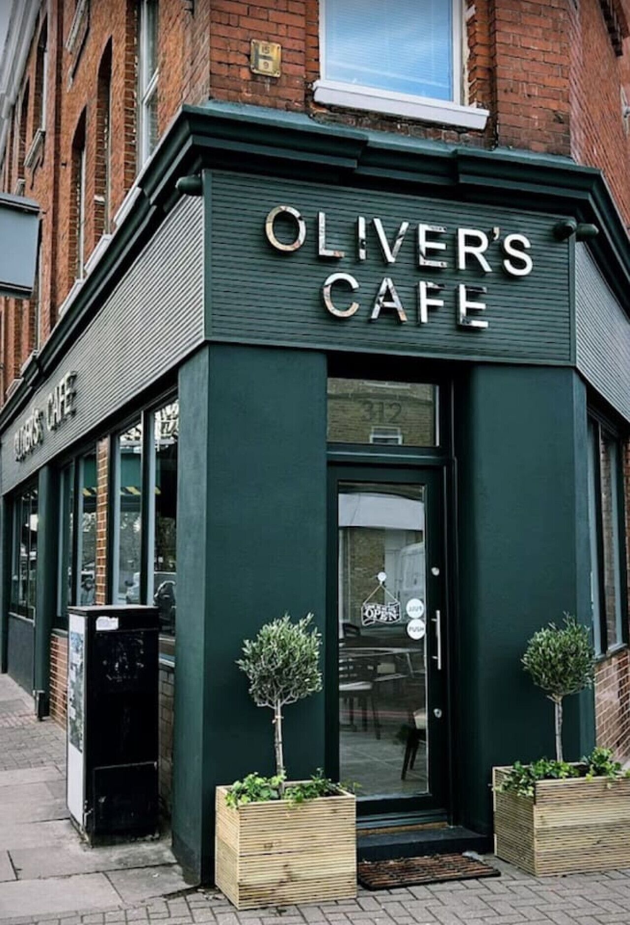 A corner building with 'OLIVER'S CAFE' signage, a glass door, and two small trees in front.