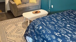 Una habitación con un sofá gris, una colcha azul estampada, un adorno redondo en la pared y un televisor montado.
