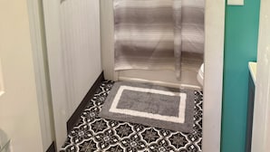 Un baño con cortina de ducha, un cuadro en la pared y un tapete estampado en el suelo.