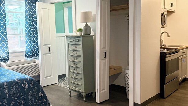Una habitación pequeña con cama, cómoda, escritorio y kitchenette.