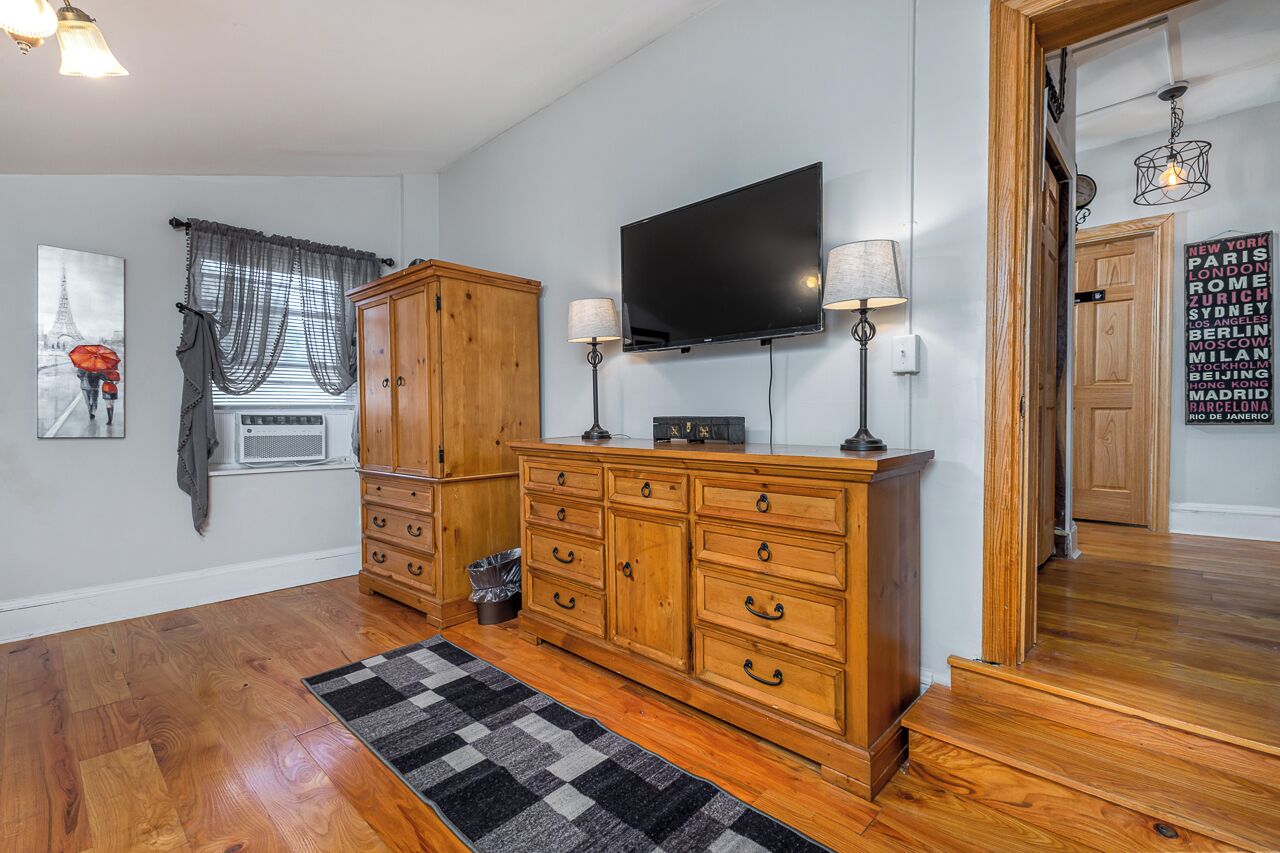 Een kamer met een houten kast, een flatscreen televisie en een zwart-wit schaakbordtapijt.
