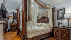 A four-poster canopy bed with a wooden frame and a canopy, a bedside table with a lamp, and a framed picture on the wall. - Majestic & Relaxing Home w/ 3 Beds Pool Table Bar! Sleeps 8 (Dubuque)
