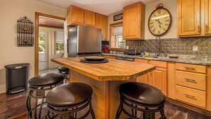 A kitchen with wooden cabinets, a stainless steel refrigerator, a clock, and a bar area with stools. - Majestic & Relaxing Home w/ 3 Beds Pool Table Bar! Sleeps 8 (Dubuque)