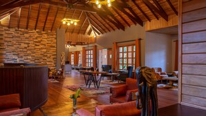 A spacious lobby with a stone wall, wooden ceiling beams, and a large statue. - Chimpundu Lodge (Fort Portal)