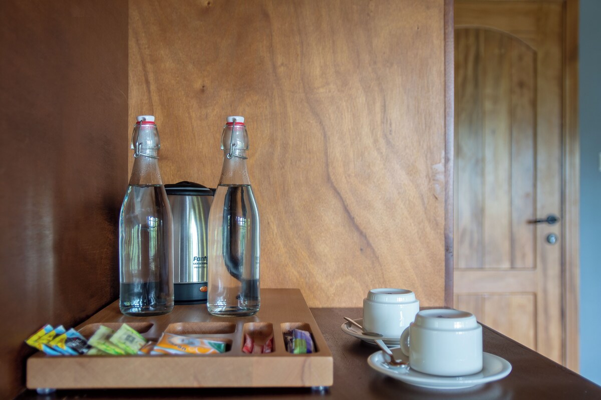Una mesa de madera con dos botellas transparentes, una bandeja con varios objetos y dos tazas blancas sobre platillos.