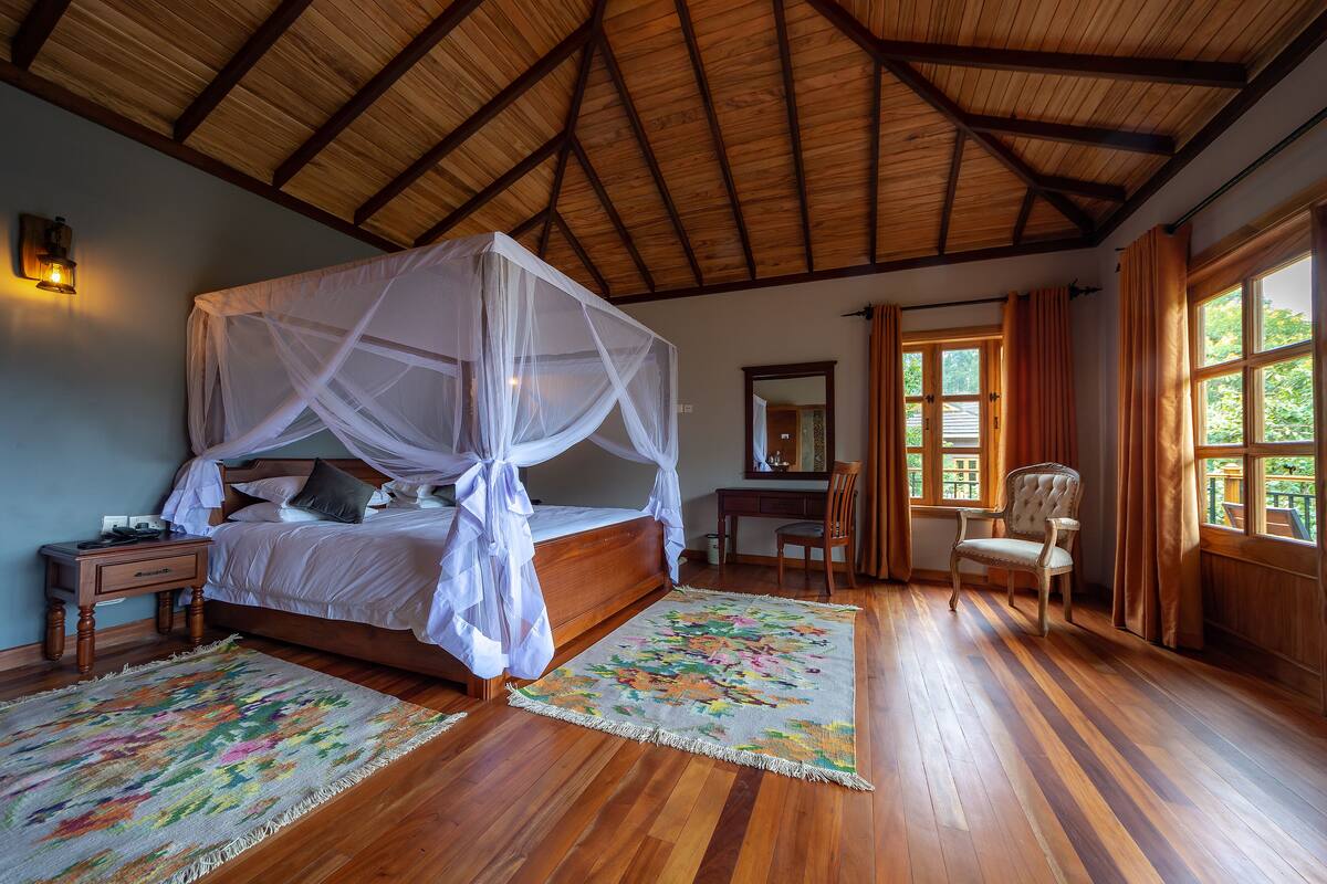 A bedroom with a four-poster bed, wooden flooring, a desk, and a chair.