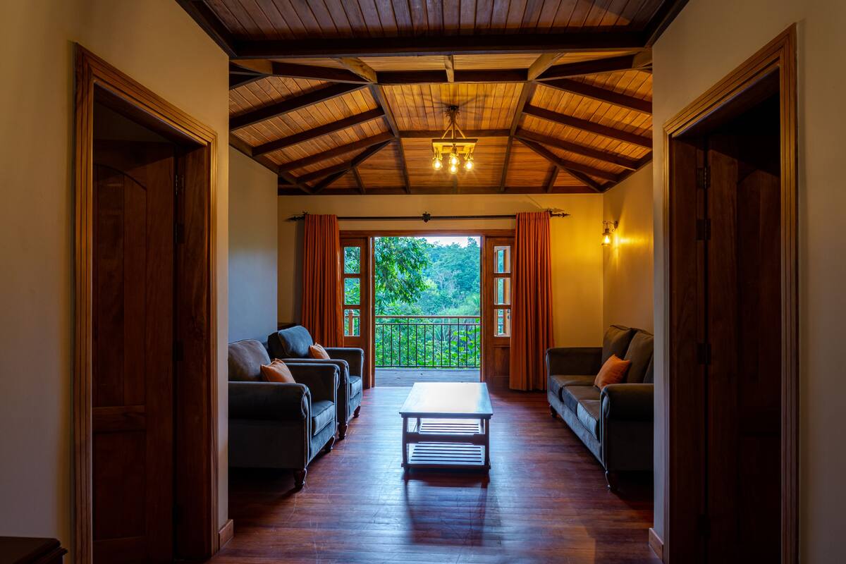 A hallway with wooden flooring, a central table, and two sofas facing a balcony with a view of greenery.