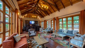 A spacious living area with wooden beams, large windows, and a bar area in the background. - Chimpundu Lodge (Fort Portal)