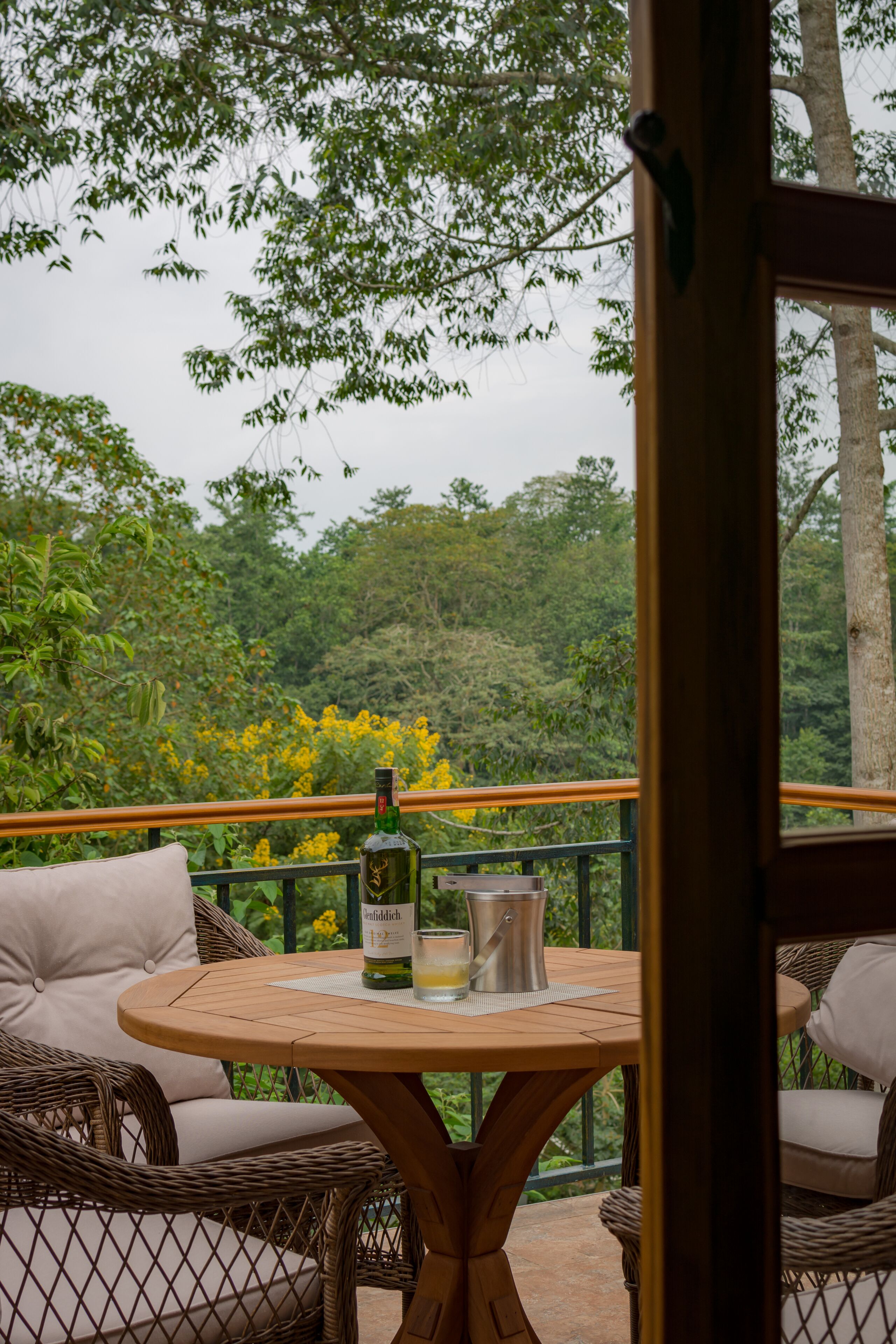 An outdoor seating area with wicker furniture and a table, overlooking a lush forested area.