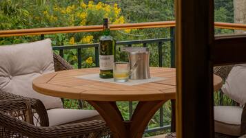 An outdoor seating area with wicker furniture and a table, overlooking a lush forested area.
