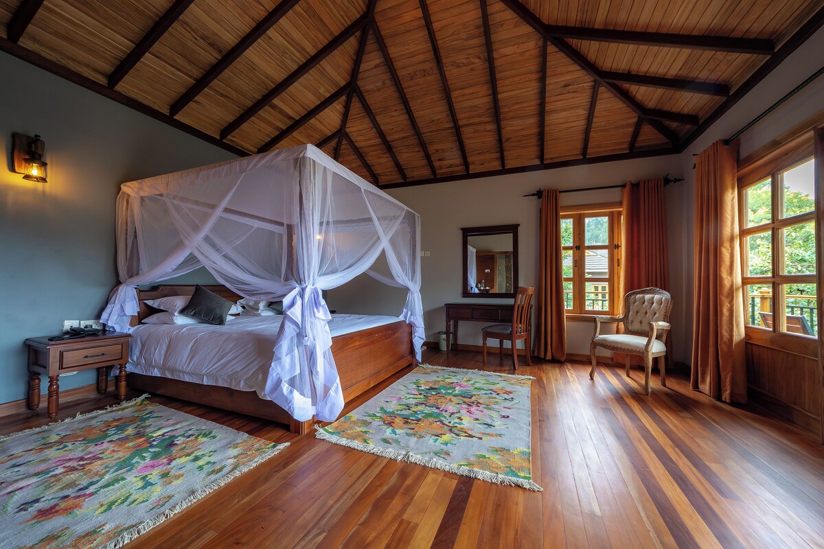 A bedroom with a four-poster bed, wooden flooring, a desk, and a chair.