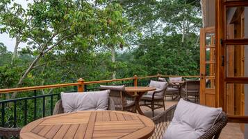 Una terraza de madera con mobiliario de mimbre y vistas a vegetación exuberante.