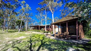 Een rustieke houten chalet met een overdekte veranda en zithoek, omgeven door een natuurlandschap met bomen en rotsen.