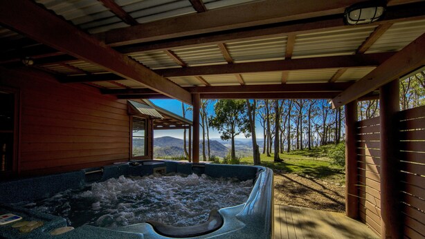 Een hottub onder een houten pergola, met uitzicht op bomen en bergen.