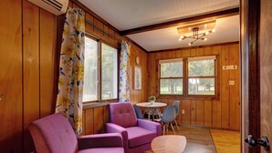 Una habitación con paredes de madera, un sofá púrpura, una pequeña mesa redonda y dos sillas.