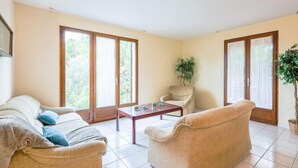 A spacious living room with a beige sofa, a wooden coffee table, and a chair. There are large sliding glass doors with a view of greenery outside. - La Maison d'Antoine by Interhome (Salles d'Aude)