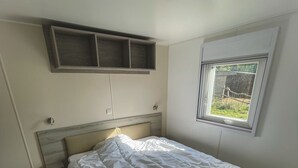 A bedroom with a bed, a window, and a built-in shelf above the bed. - Charming mobile home in the heart of nature (Vidauban)