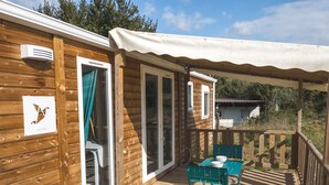 A wooden deck with a covered seating area, a table, and a chair. - Charming mobile home in the heart of nature (Vidauban)