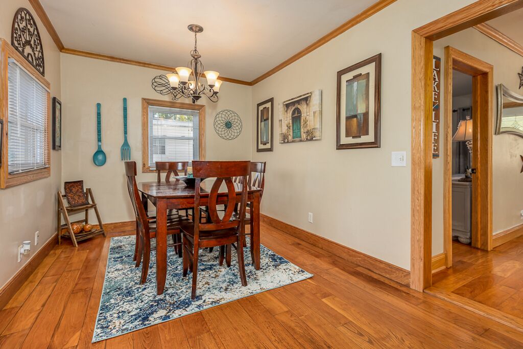 A dining area with a wooden table and chairs, a chandelier, and framed artwork on the walls.