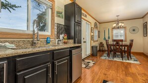 A kitchen with dark cabinets, a granite countertop, a refrigerator, and a dining area with a table and chairs.