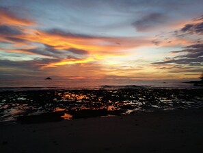 Uma praia ao pôr do sol, com céu limpo e mar calmo.