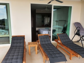 Quarto com três poltronas de madeira com almofadas pretas, uma mesa de madeira pequena e um ventilador de teto.