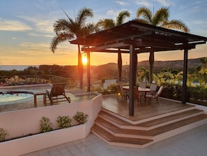 Terraço no telhado com piscina, área de estar externa e vista do pôr do sol sobre o oceano.