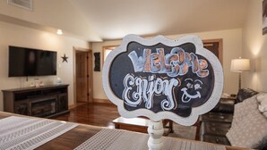 Una habitación con una mesa de madera, un televisor montado en la pared y un cartel que dice 'Welcome Enjoy'.