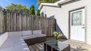 Un patio cubierto con un sofá seccional, una mesa con superficie de vidrio y una terraza de madera.
