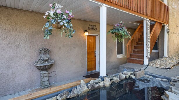 A building with a wooden balcony, a welcome sign, a stone planter, and a small pond.