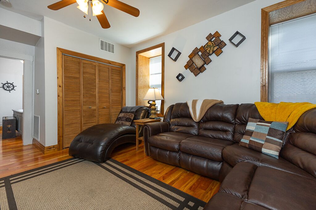 A living room with a leather sofa, wooden floor, and a ceiling fan.