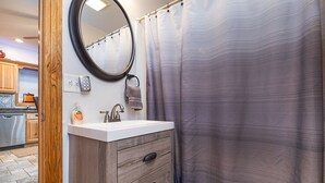A bathroom with a wooden vanity, a round mirror, a white sink, and a striped shower curtain.