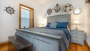 A bedroom with a wooden headboard, a bed with blue bedding, a chest of drawers, and nautical-themed wall decor.