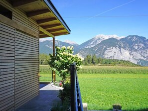 A wooden building with a balcony overlooking a green field and mountains.